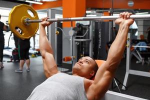 Lying man lifting barbell in gym photo