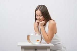 girl sits near aquarium with goldfish and looks at it photo