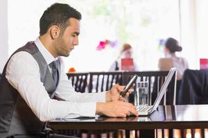 Serious businessman using phone while working on laptop photo