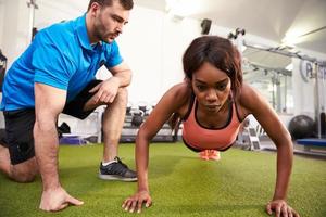 Young woman doing push ups under supervision of a trainer photo