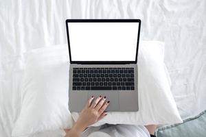Top view mockup image of a woman sitting on a bed , using and touching on laptop with blank white desktop screen  keyboard