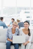 Women using laptop with colleagues in background at creative office photo