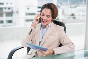 Brunette laughing businesswoman using smartphone and holding tablet photo