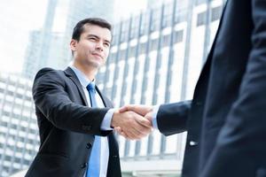Businessmen making handshake in front of office buildings in the city