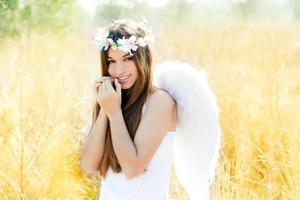 Niña ángel en campo dorado con alas de plumas blancas foto