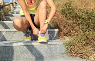 young woman runner tying shoelaces on stone trail