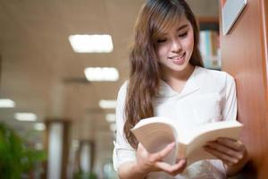 Hermosa asiática estudiante leyendo libro en biblioteca foto