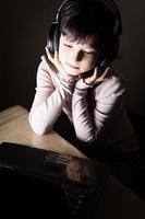 Girl with headphones using laptom in dark room photo
