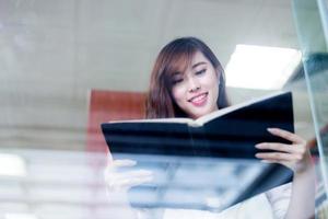 Estudiante asiática hermosa que sostiene el libro en retrato de la biblioteca foto