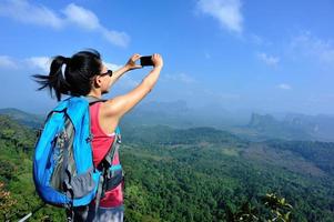 hiking woman taking photo with smart phone on mountain peak