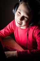 Girl with headphones using laptom in dark room listening music