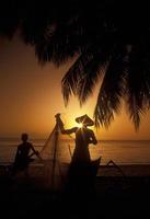 siluetas de pescadores, indonesia, en la playa tropical al atardecer foto