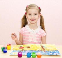 Cute smiling little girl drawing with paint and paintbrush photo