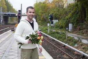 man waiting at train station with flowers