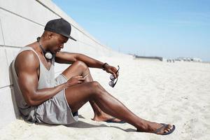 Young african guy sending a text message at the beach photo