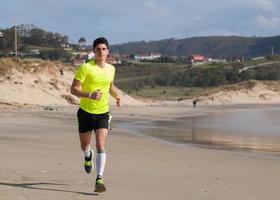Young Man In Fitness Clothing Running Along Beach photo