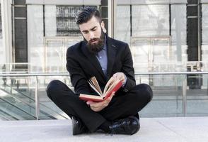 young hipster reading a book sitting outdoors photo