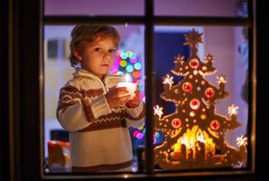 Happy little child standing by window at Christmas time photo