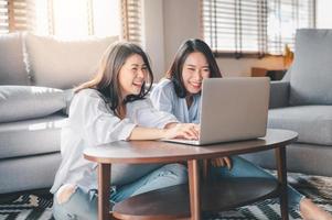 Two Asian women laughing while working with laptop at home photo