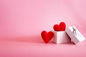 Dos corazones rojos en una caja de regalo sobre fondo rosa foto