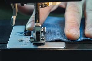 Male hand sewing denim on a sewing machine