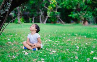 linda niña asiática sentada en el parque y mirando hacia arriba foto