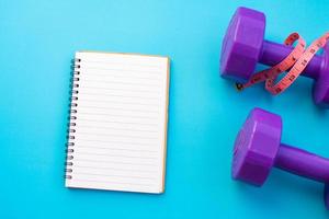 Dumbbells with notepad on blue background photo