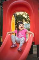 Little girl slides down red playground slide photo