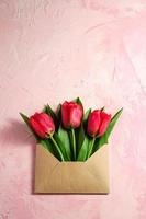Flores de tulipán rojo en sobres de papel sobre fondo rosa con textura