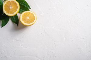 Two lemon slices with green leaves on white concrete background photo