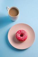 Pink donut with sprinkles on plate next to coffee photo