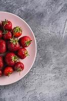Ripe strawberries on plate against grey stone background