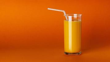 Un vaso de jugo de naranja sobre fondo naranja con espacio de copia foto
