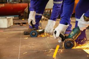 Two workers cut metal sheets with electric grinder photo