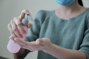 Mujer aplicando gel antiséptico de alcohol y usando mascarilla foto