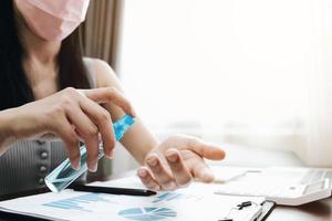 Woman sanitizing hands and wearing face mask in home office photo