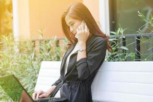 Young professional Asian woman uses her laptop and phone on a bench photo