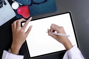 Doctor mano escribiendo en la pantalla de la tableta mientras está sentado en el escritorio.