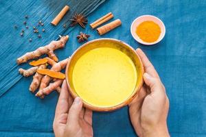 Hands holding golden milk or turmeric latte with ingredients photo