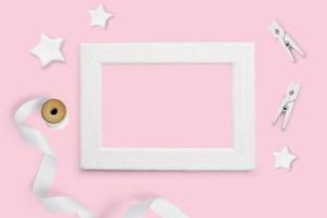 Mockup of white wooden frame, white stars, ribbon, and clothespins photo