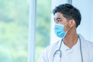 Man with face mask and stethoscope looking out window photo
