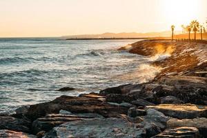 Waves splashing on rocky beach during golden hour photo