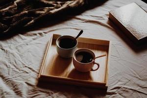 Cups of coffee on wooden tray on bed photo