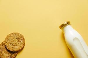 Two cookies and a bottle of milk on yellow background photo