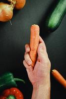 Hand holding carrot surrounded by vegetables photo