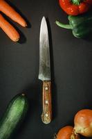 Chef knife surrounded by vegetables on dark background