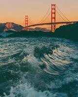 Ocean waves crashing in the foreground with the Golden Gate Bridge in the background 