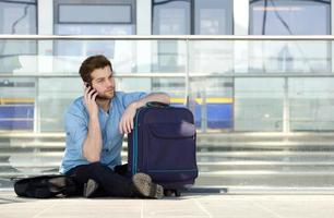 Male traveler sitting on floor talking on mobile phone photo