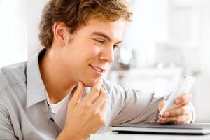 Joyful young man using mobile phone at home is happy