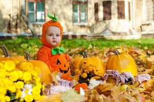 Niño en traje de calabaza sobre fondo de hojas de otoño foto